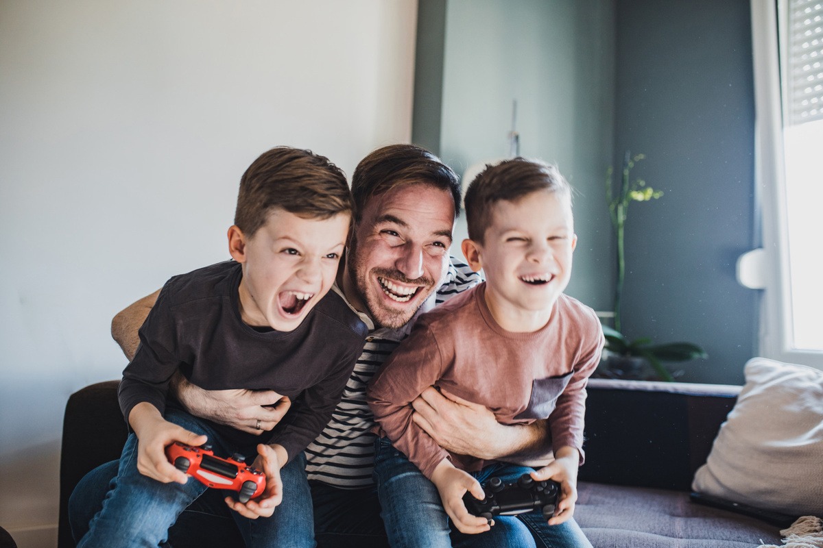 Un pere joue a la console video avec ses enfants.