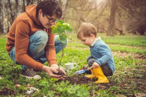 Un jeune pere aide son enfant a planter un arbre.