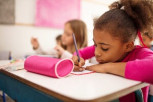 Une jeune ecoliere ecrit sur son cahier de classe.